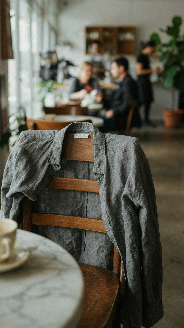 A grey linen shirt with natural wrinkles draped over a cafe chair.