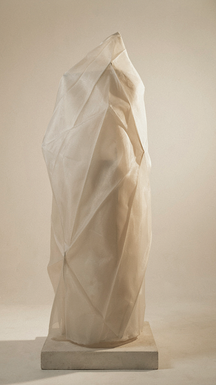 A large organza fabric sculpture shows crisp folds and geometric lines in bright light.