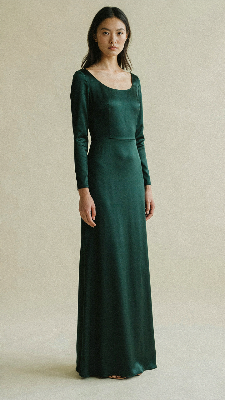 A woman in a dark green gown stands still with subtle confidence.