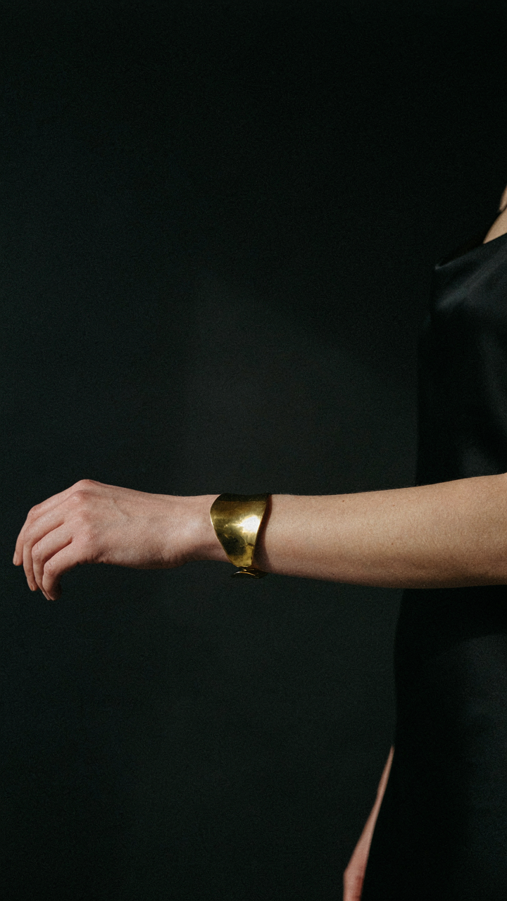 A gold cuff bracelet stands out against a black dress.
