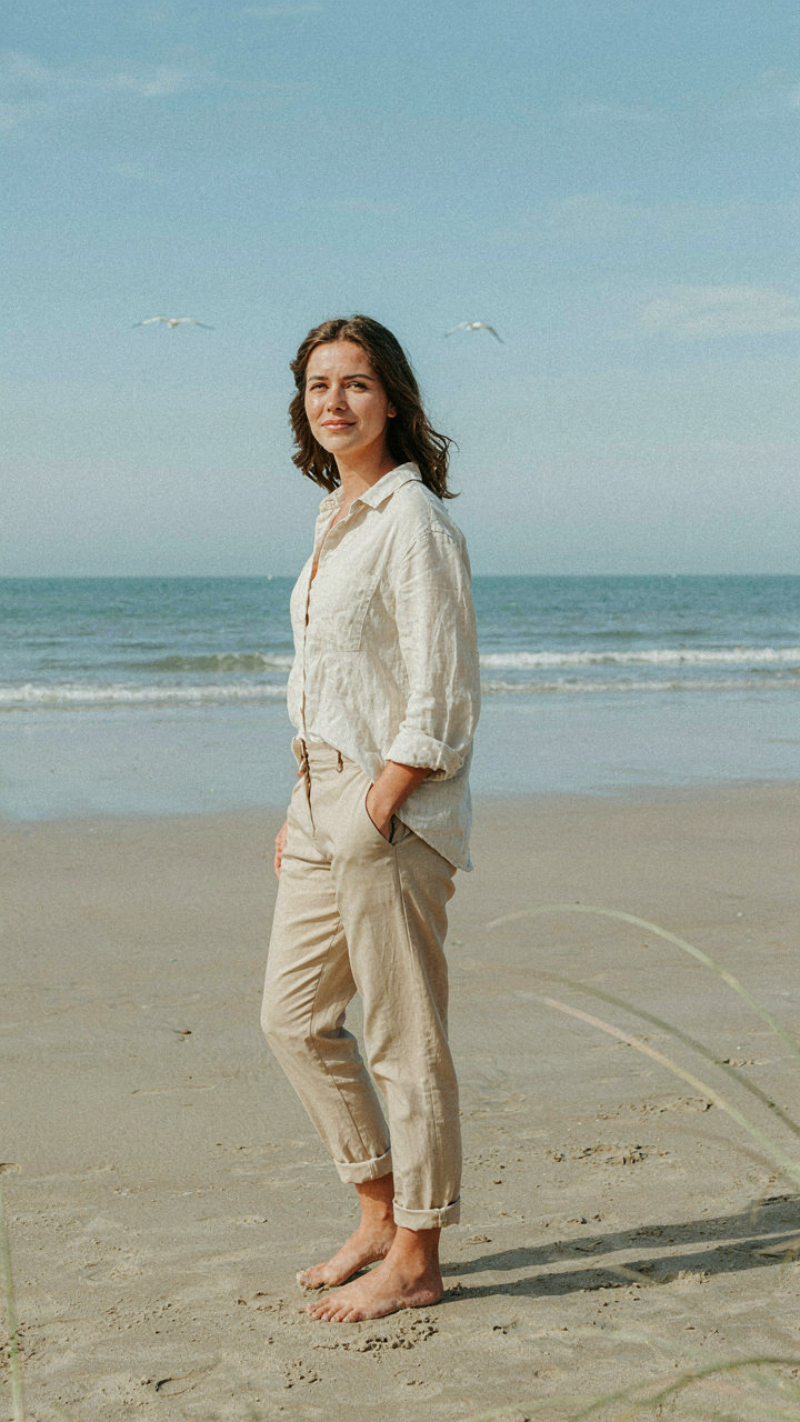 A person in loose linen and cotton clothing stands calmly on a beach.