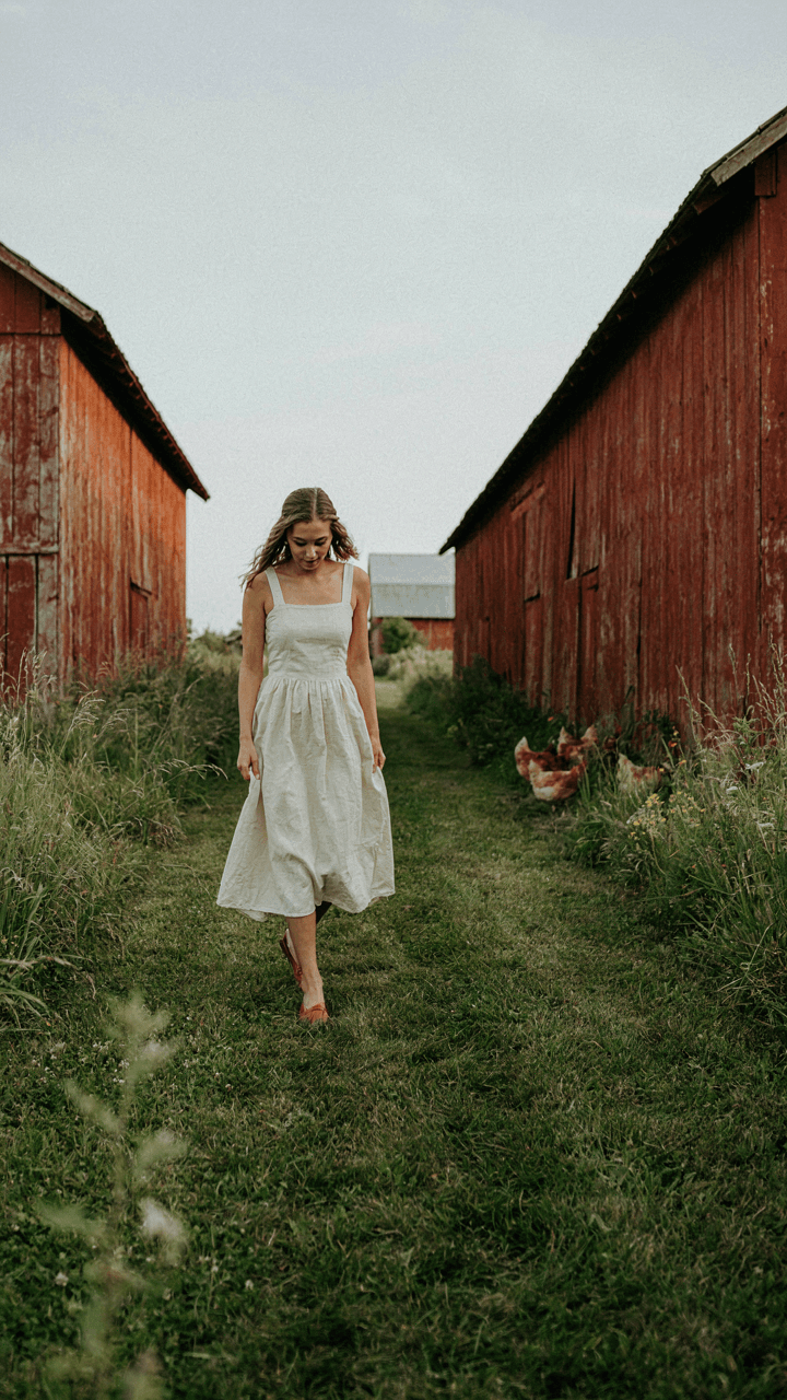 A woman in a dress and flats walks on an uneven grassy path.