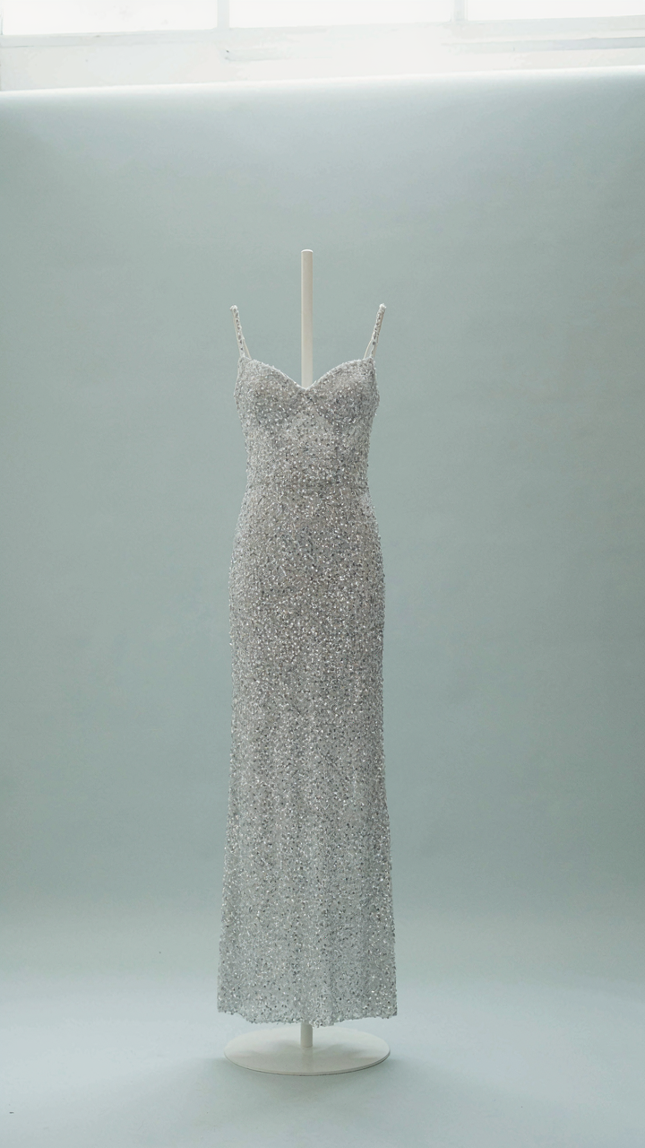 A single elegant sequin cocktail dress on a minimalist stand.