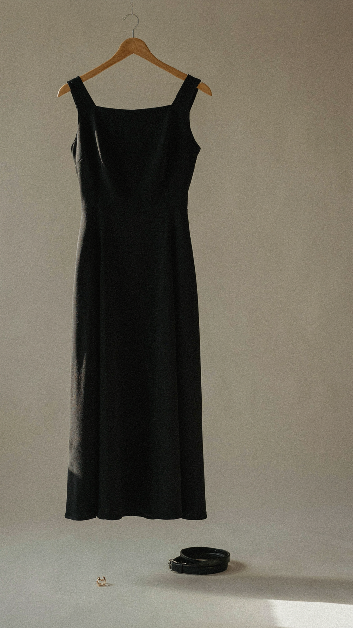 A classic black midi dress with a square neckline hangs on a wooden hanger.