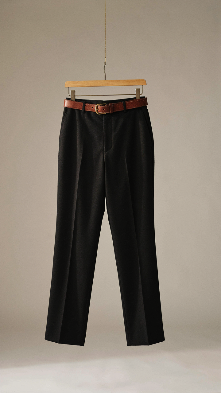 Well-fitted black wool trousers with a cognac leather belt on a hanger.