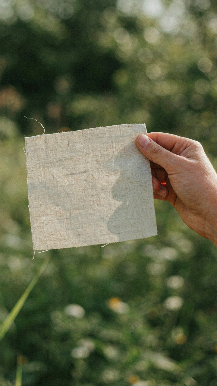 Hand holds light linen fabric to sun, showing visible weave and transparency.