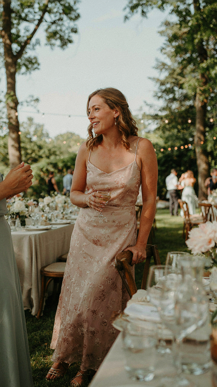A smiling wedding guest in elegant flats, talking at a reception.