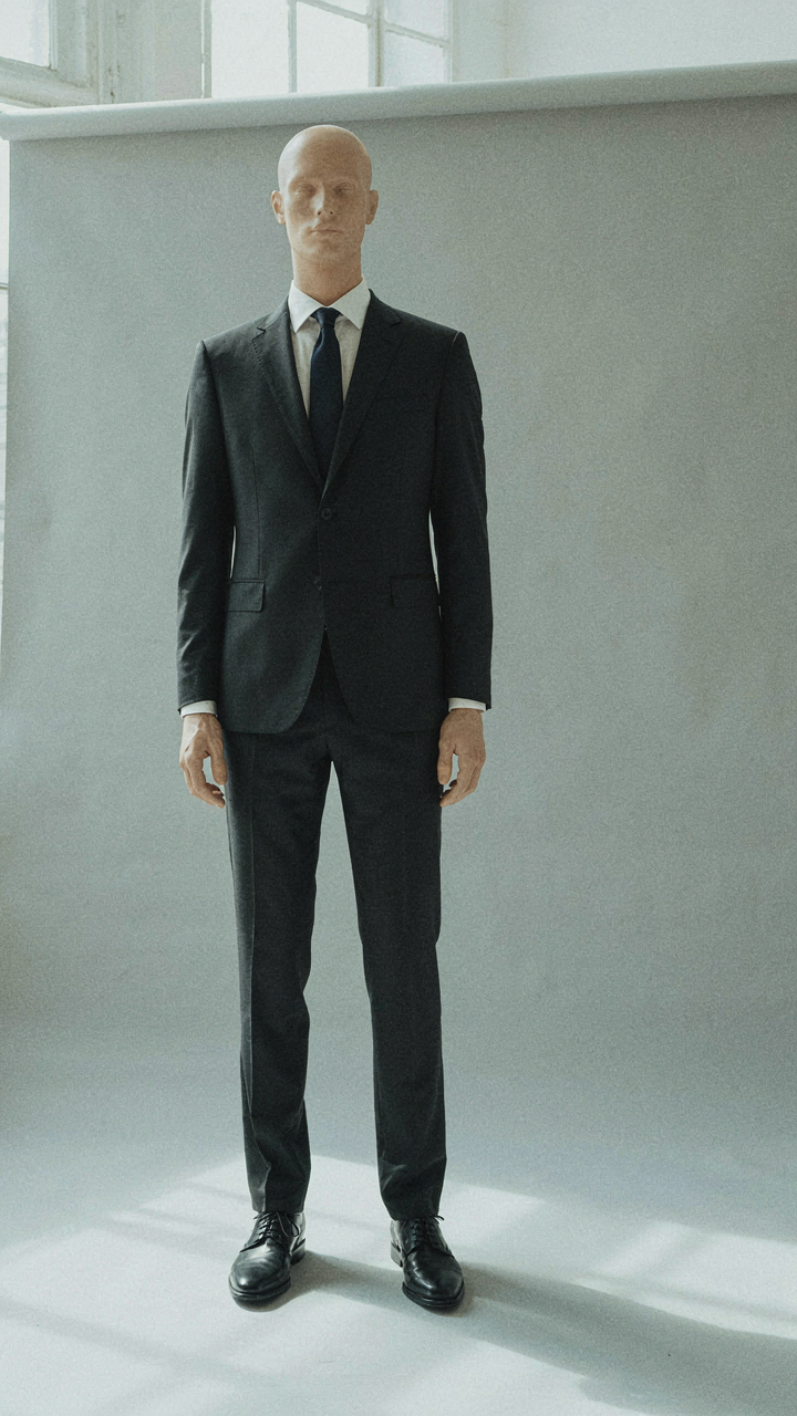 A mannequin wears a perfectly tailored dark business suit with a structured silhouette.