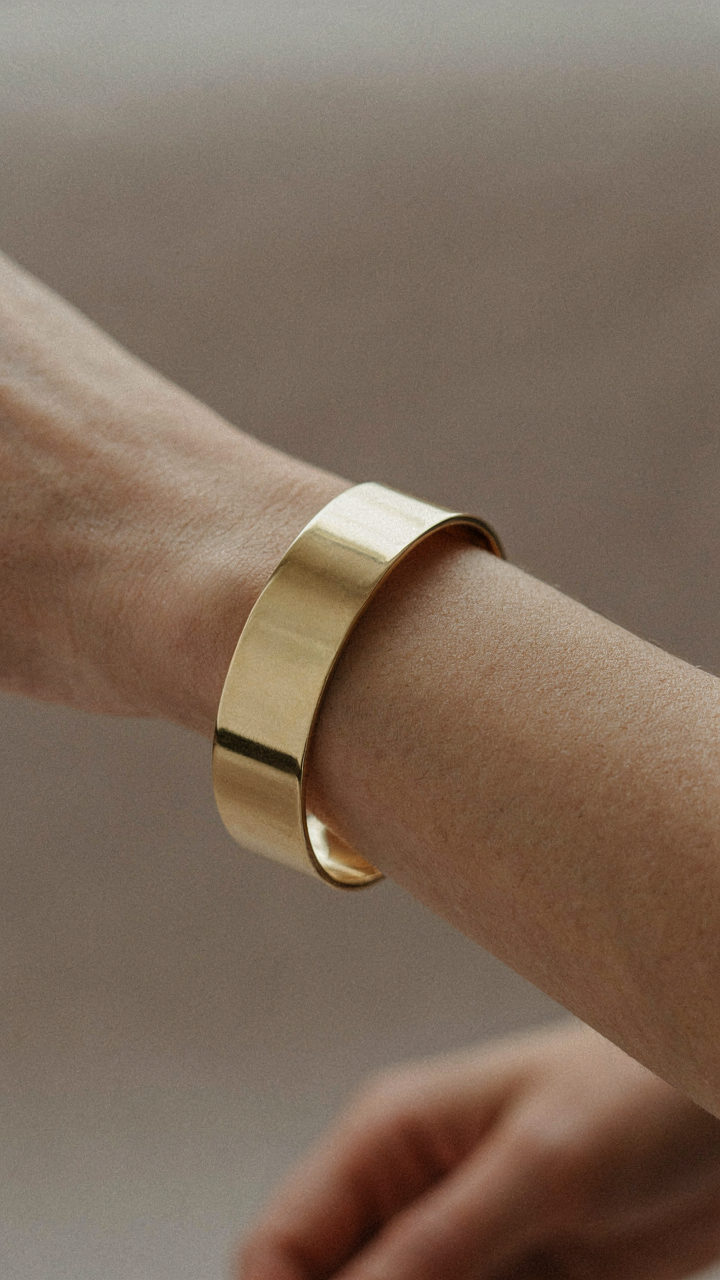 A woman's wrist with a single wide, structured gold cuff bracelet.