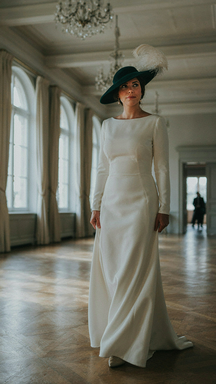 A woman in a structured dress and hat walks into a ballroom.