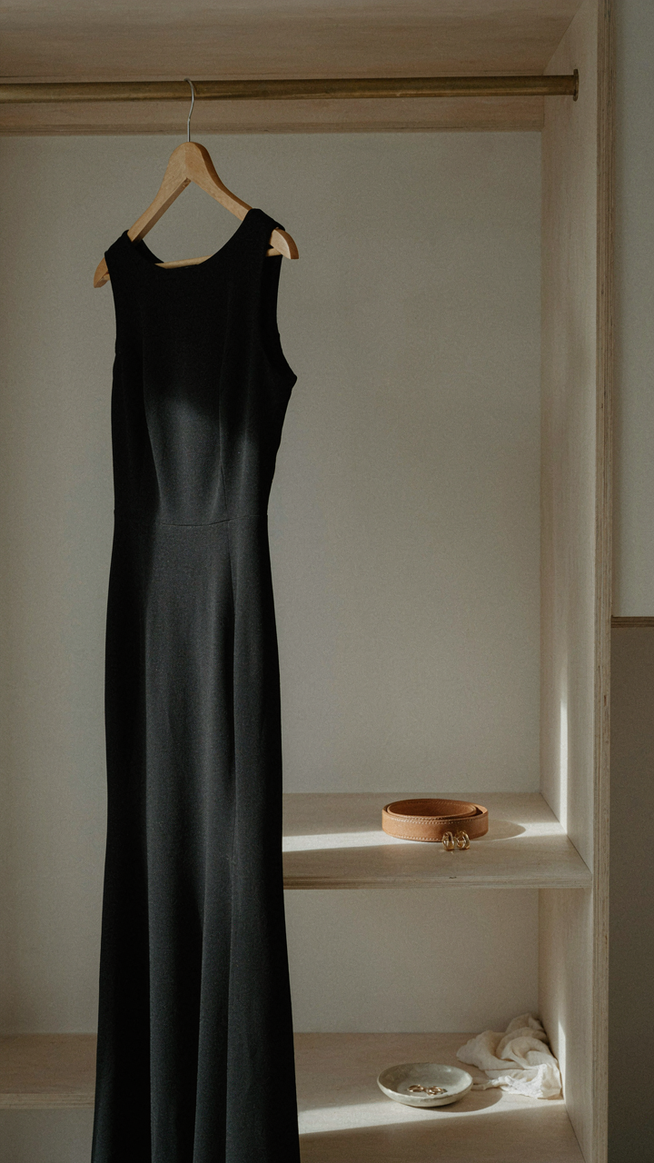 A classic black floor-length dress hangs in a sunlit wardrobe.