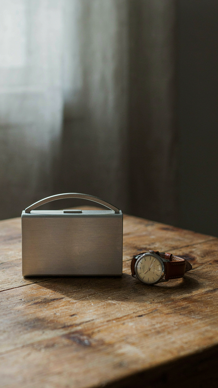 A simple, structured brushed metal clutch rests on a vintage wooden table.