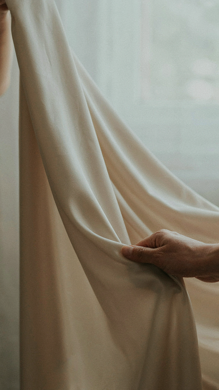 A hand gently touches a piece of flowing silk blend fabric, showing its drape.