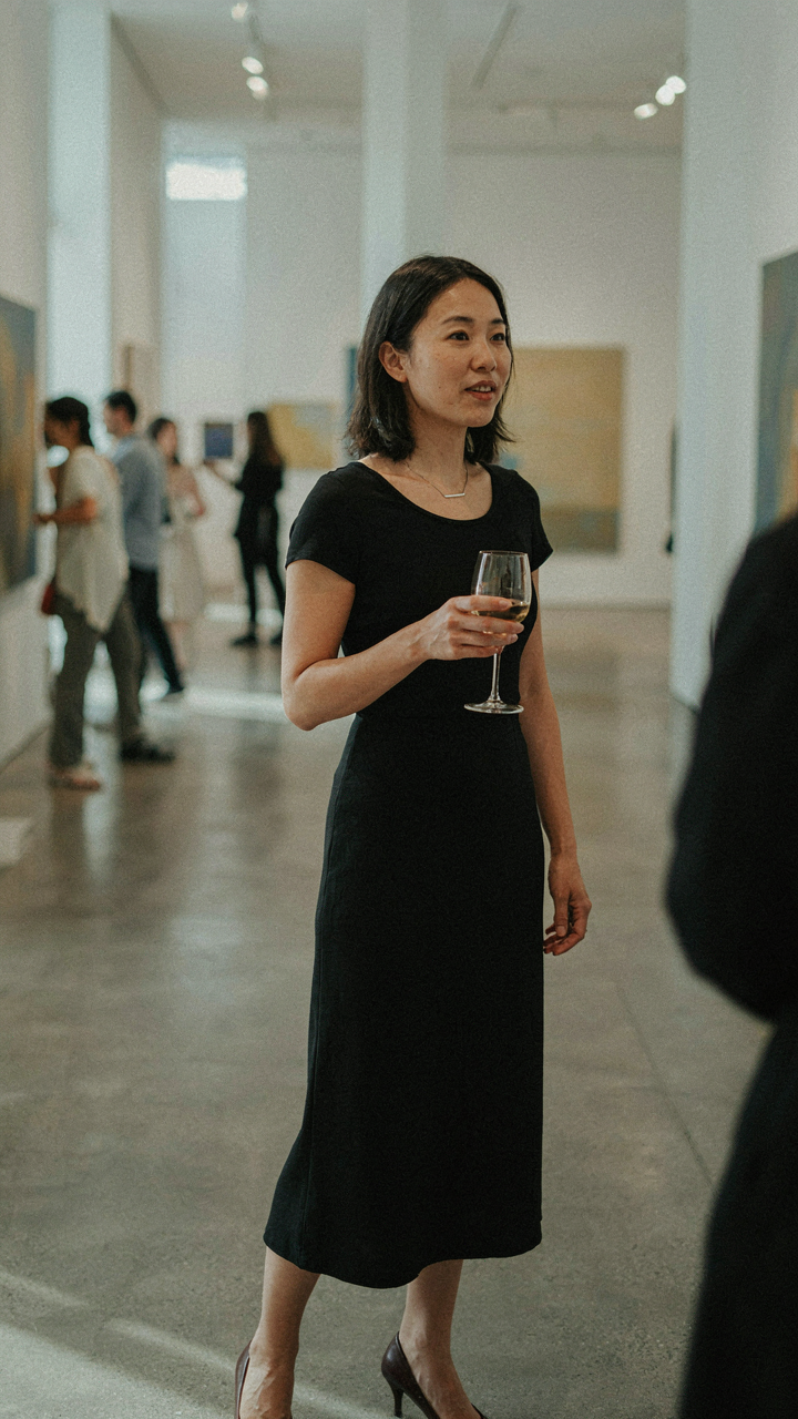 A person in an elegant black dress converses confidently in a busy gallery.