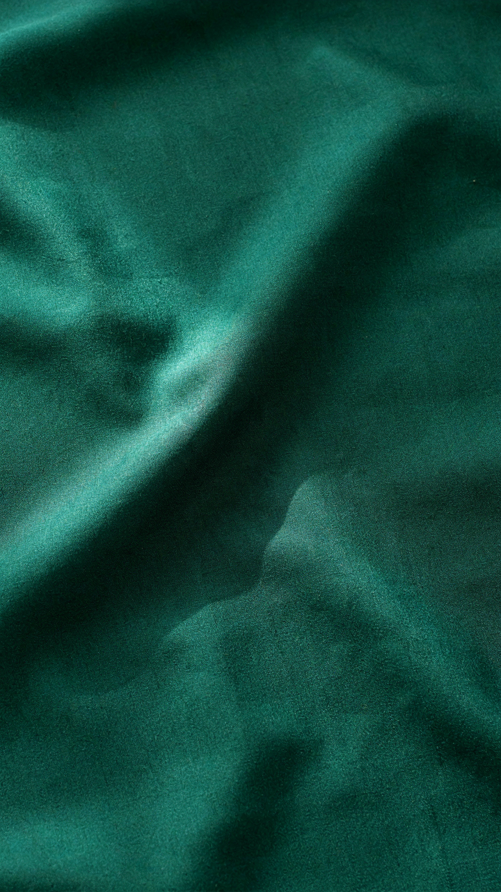 A close up of a deep emerald green structured silk fabric.