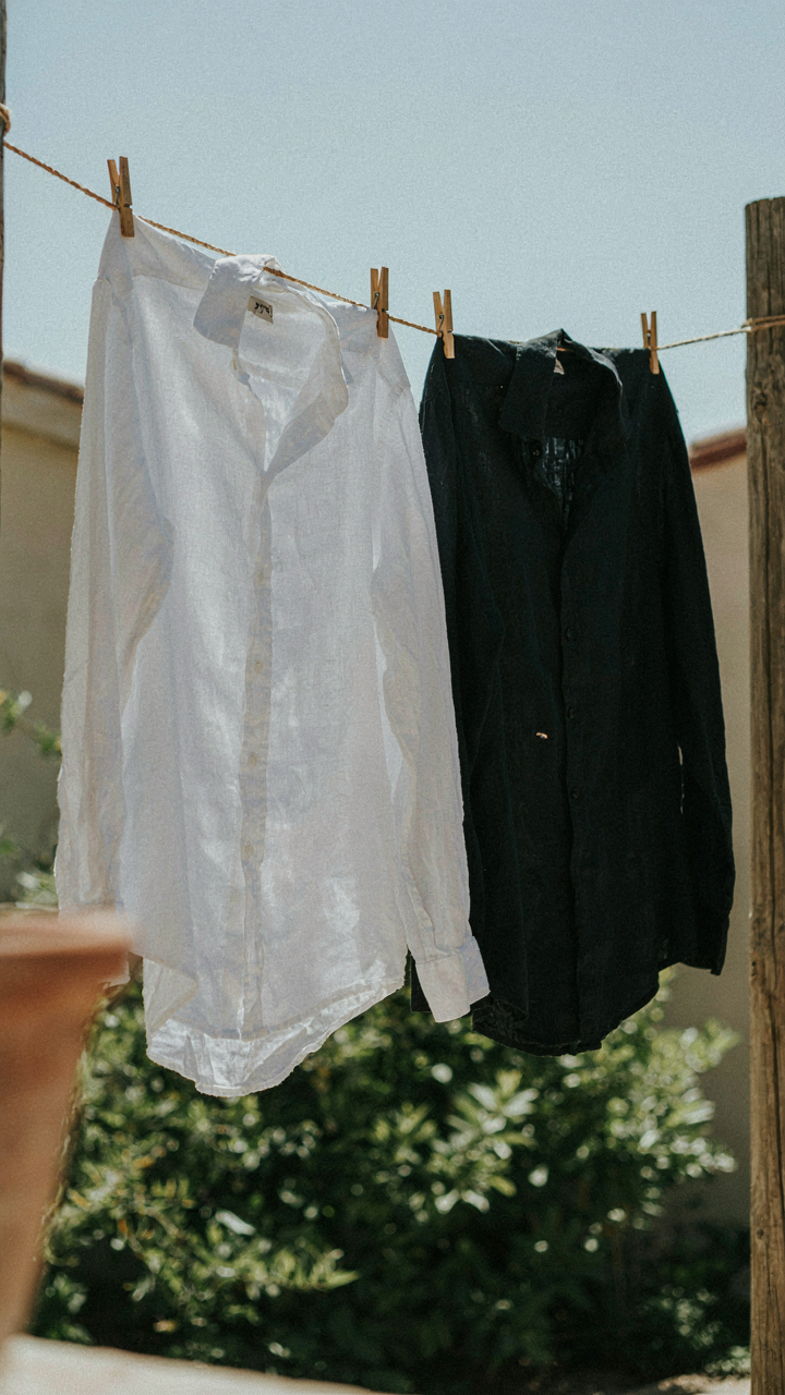 White linen shirt and black linen shirt hanging in sunlight.