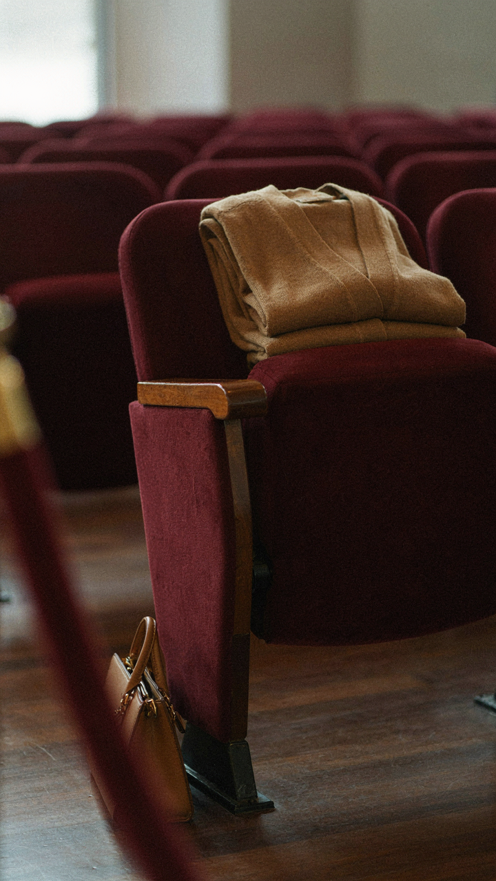 A structured cardigan folded neatly on a theater seat.