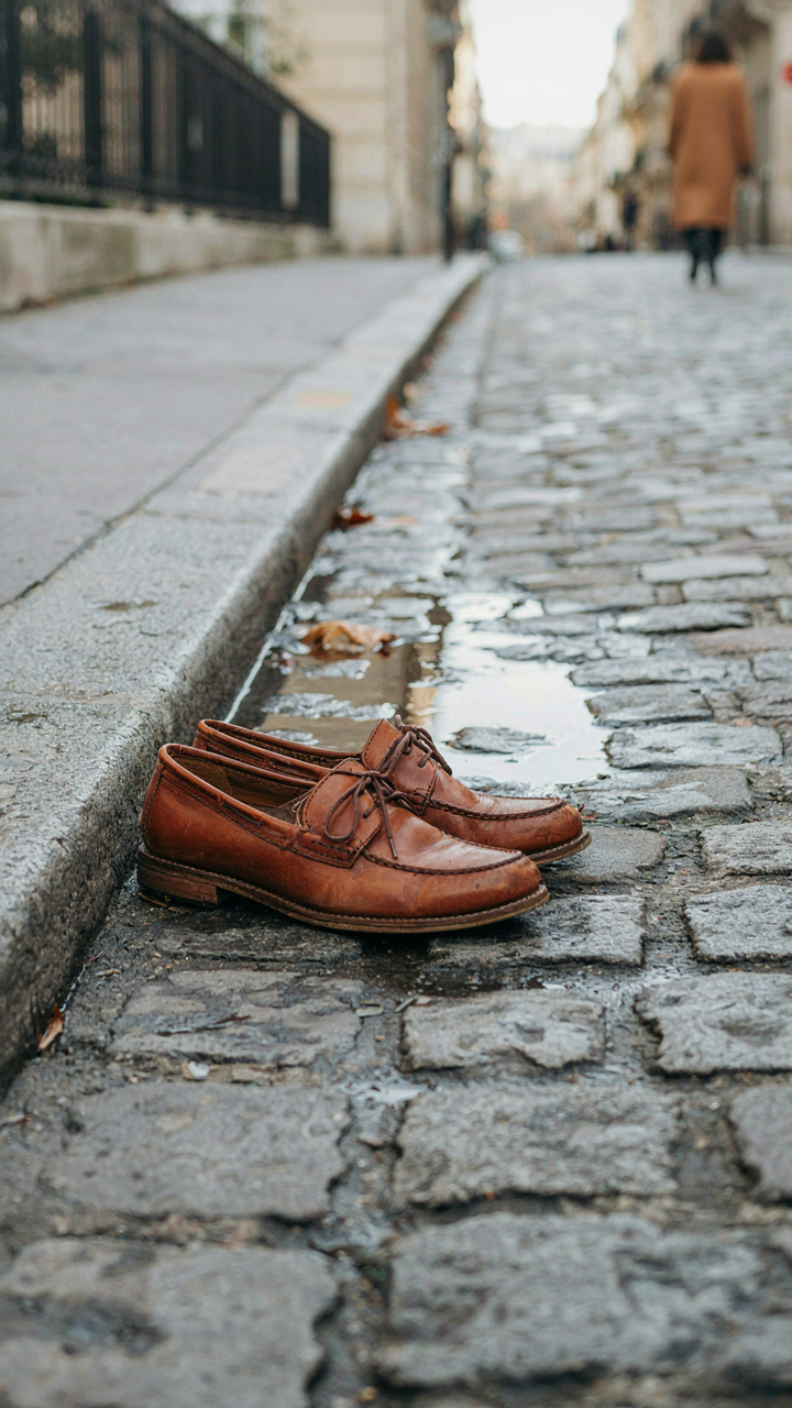 Stylish, well-worn leather loafers on a wet cobblestone street.
