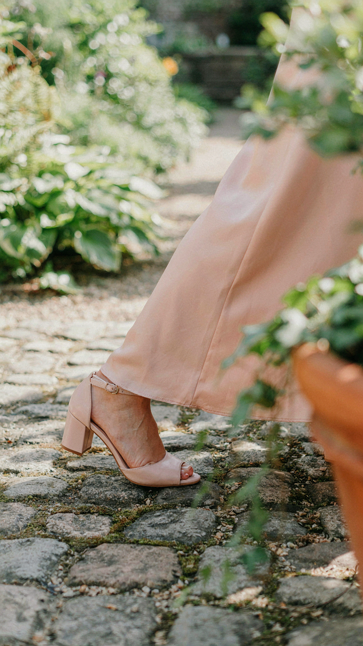 A woman in block heels walks on cobblestones, a maxi dress hem visible.