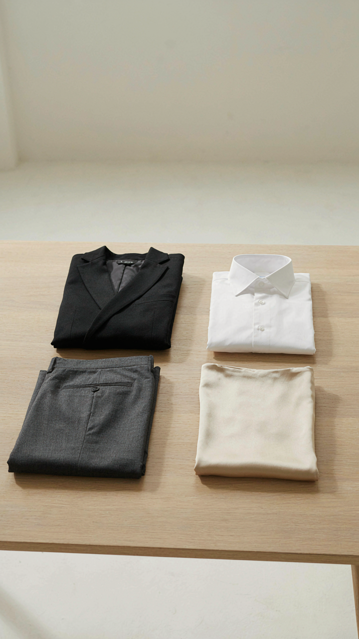 Four core clothing pieces, a blazer, white shirt, trousers, and sheath dress, on a table.