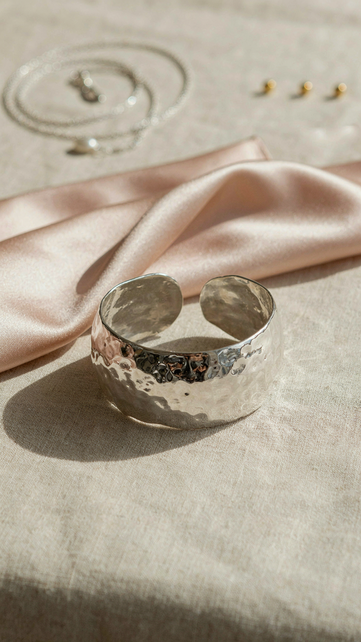 A statement silver cuff bracelet on satin fabric, with other blurred accessories.