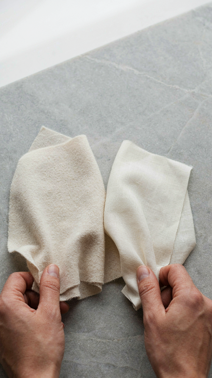 Hands feel the texture of wool and cotton fabric swatches on a stone.