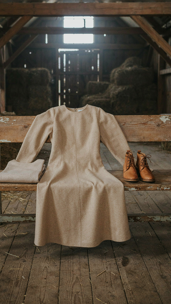 A long sleeve midi dress and boots on a wooden bench in a barn.