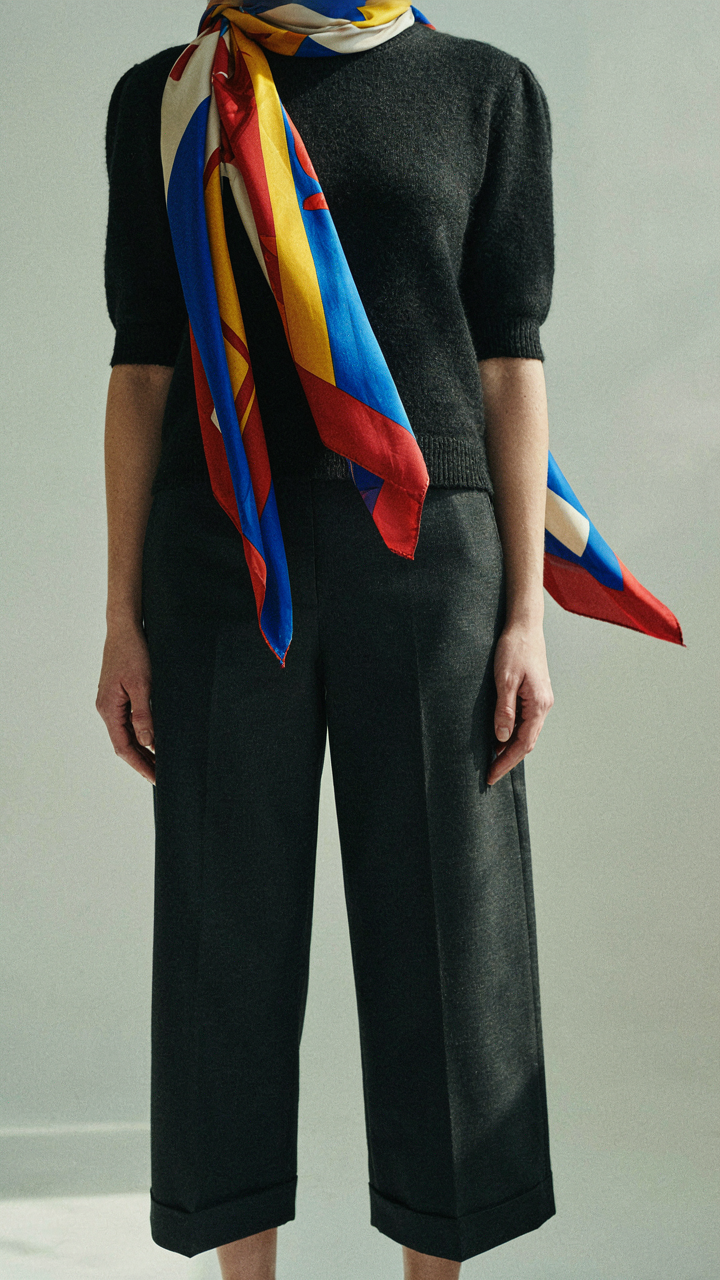 A person wears a dark matching set with a brightly patterned scarf for contrast.