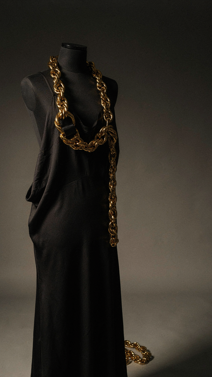 A heavy gold chain rests against a dark silk dress, showing visual contrast.