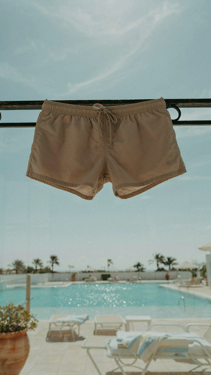 Swim trunks hanging to dry on a hotel balcony railing overlooking a pool.