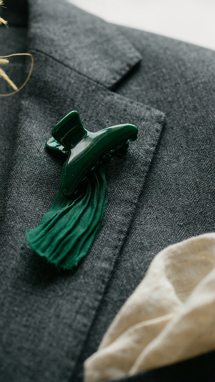 A jewel-toned silk claw clip rests on a tailored jacket, ready for a wedding guest outfit.