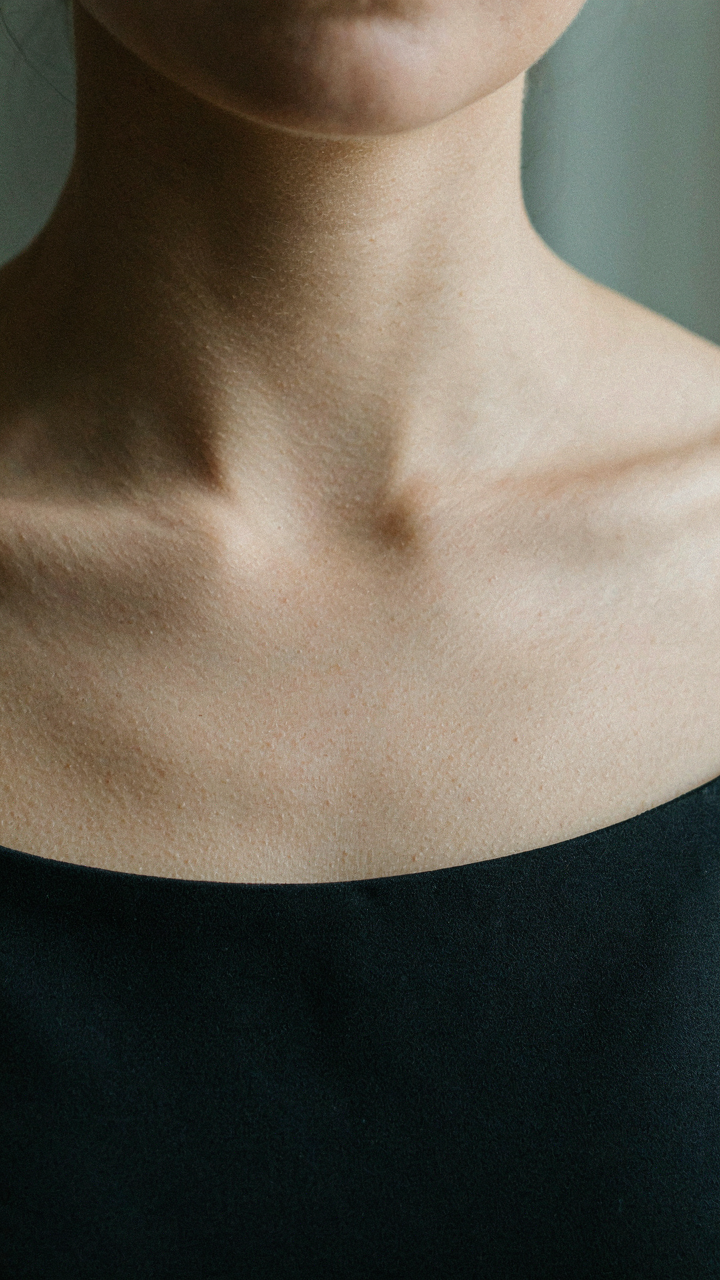 Close-up on a woman's collarbones, framed by a dark boat neck cocktail dress.