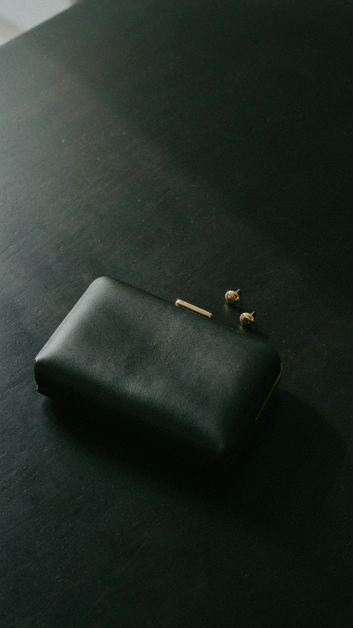 An elegant clutch bag and simple stud earrings are arranged on a dark surface.