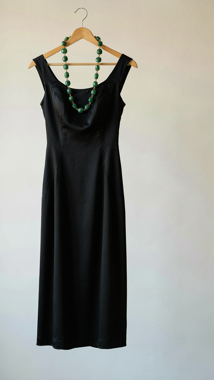 A vibrant emerald green statement necklace lies on a black silk dress.