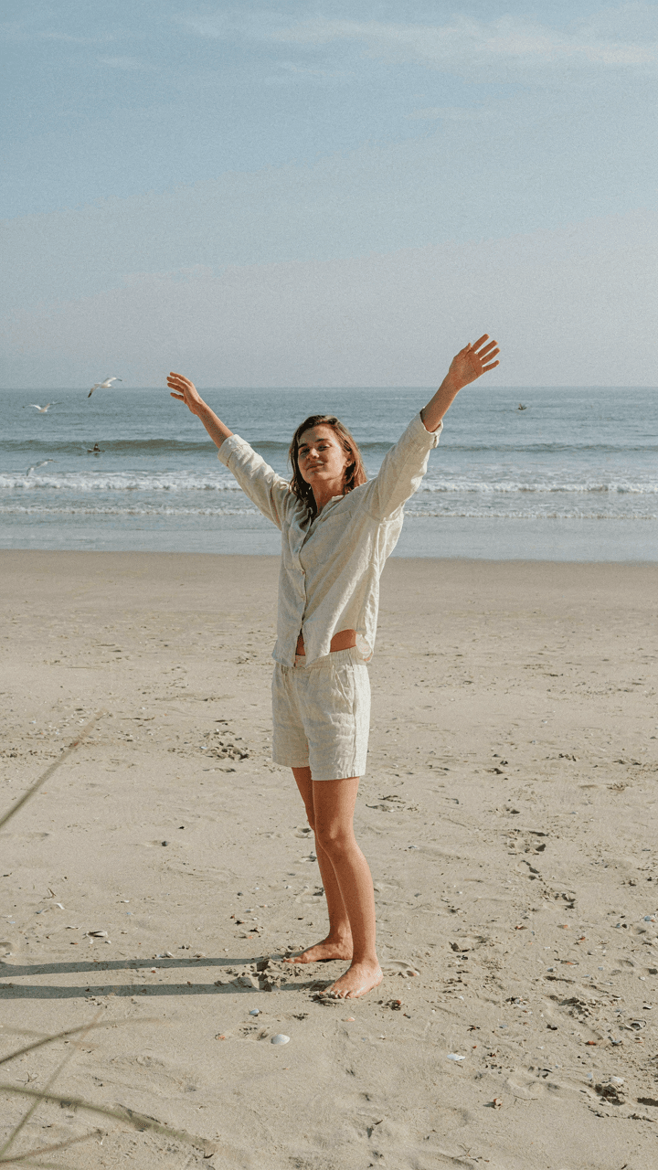 A person in a linen shirt and shorts stretches comfortably on soft sand.