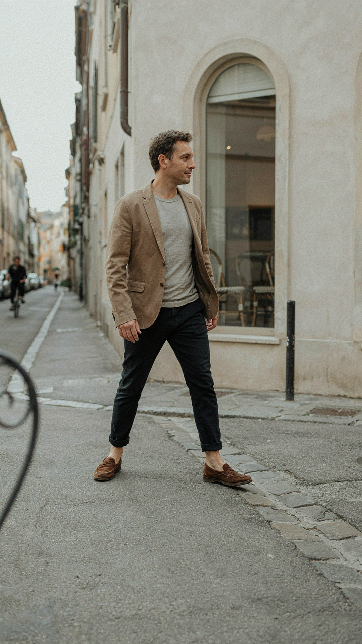 A person in a lived-in blazer and t-shirt walks past a cafe.