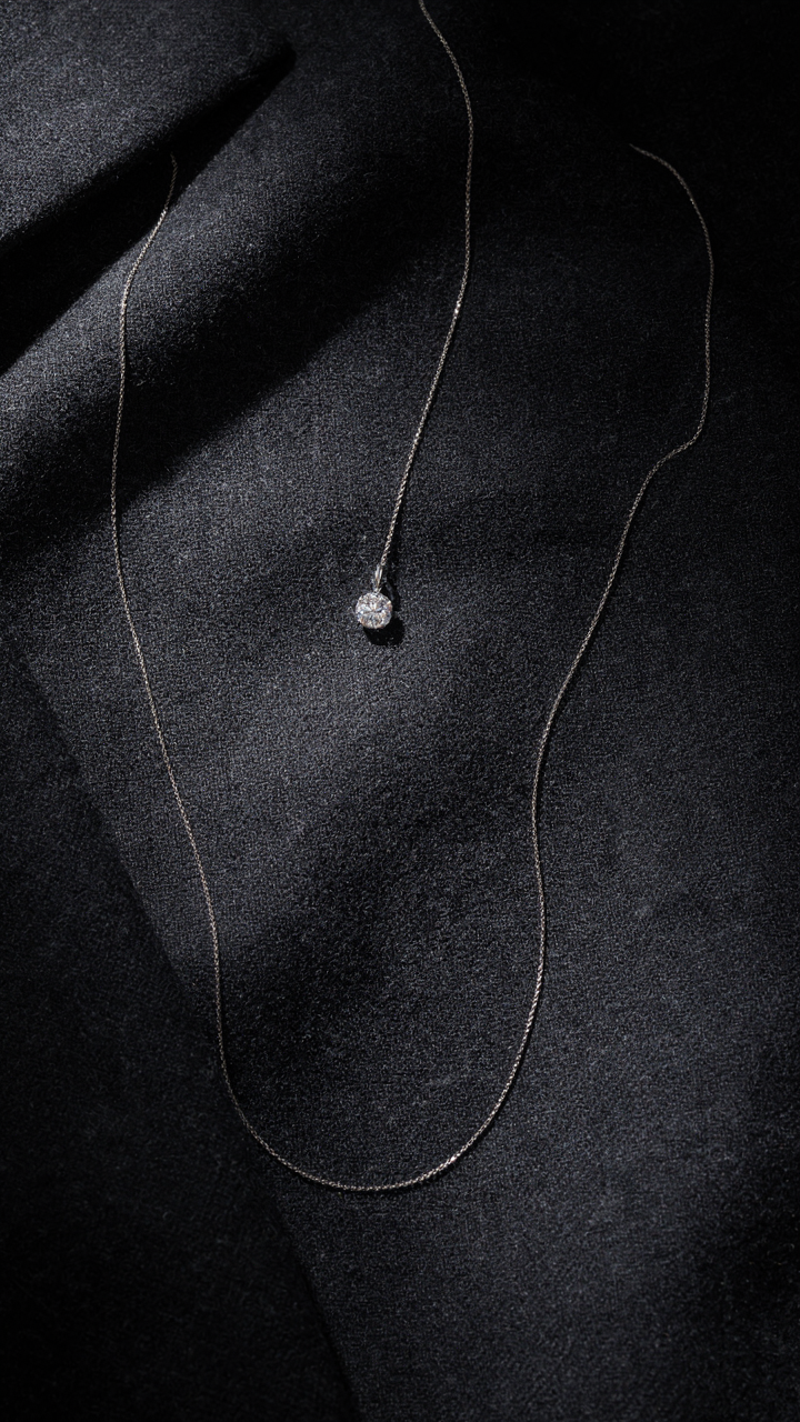 A single, elegant diamond pendant necklace on dark fabric.