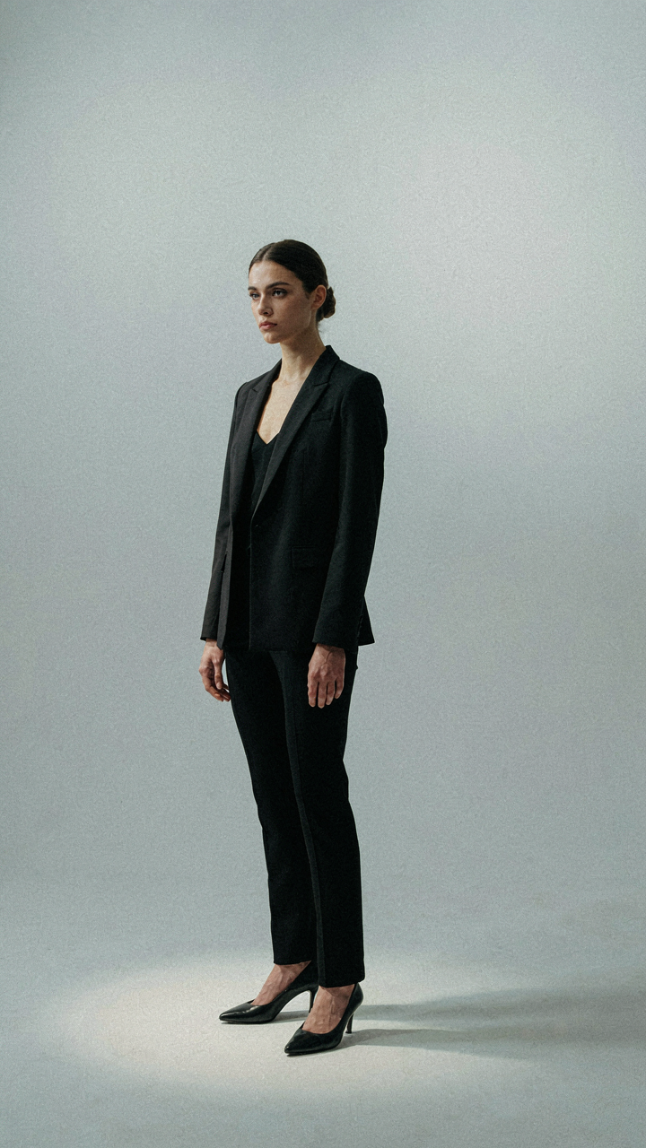 A woman in a structured blazer highlights her strong shoulders in a bright room.