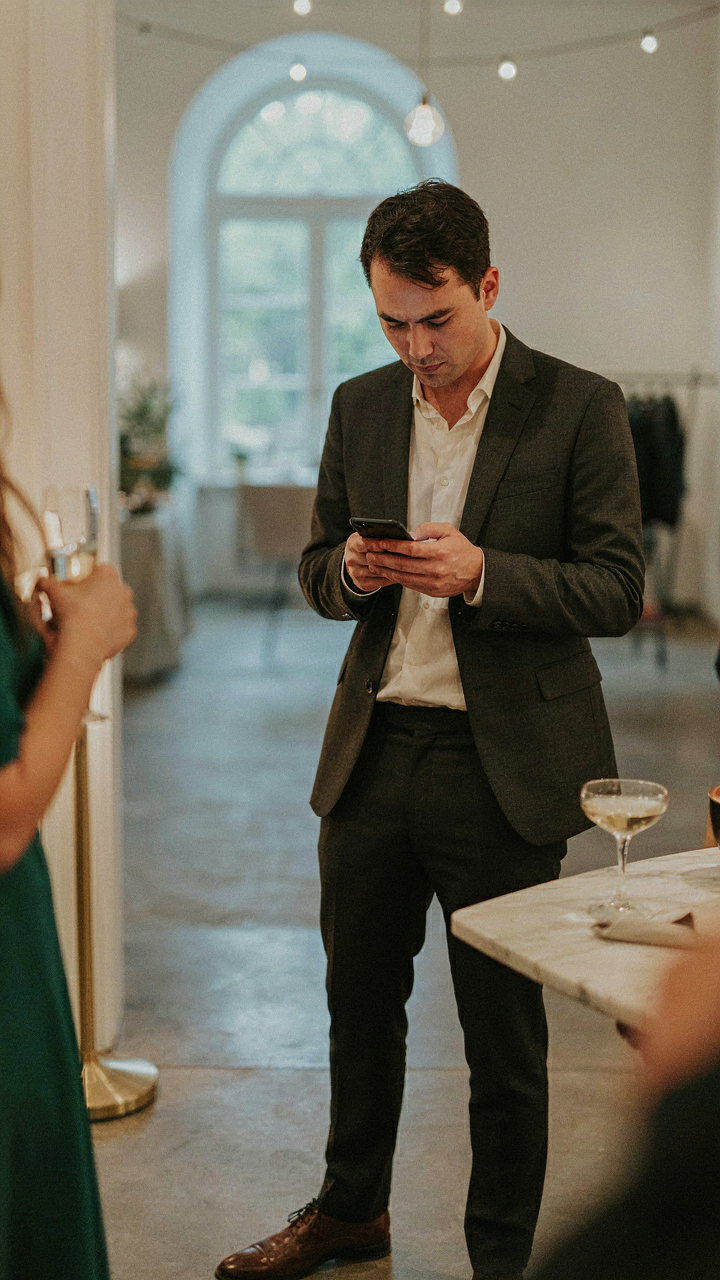 A guest subtly checks a phone for clues about a party's dress code.