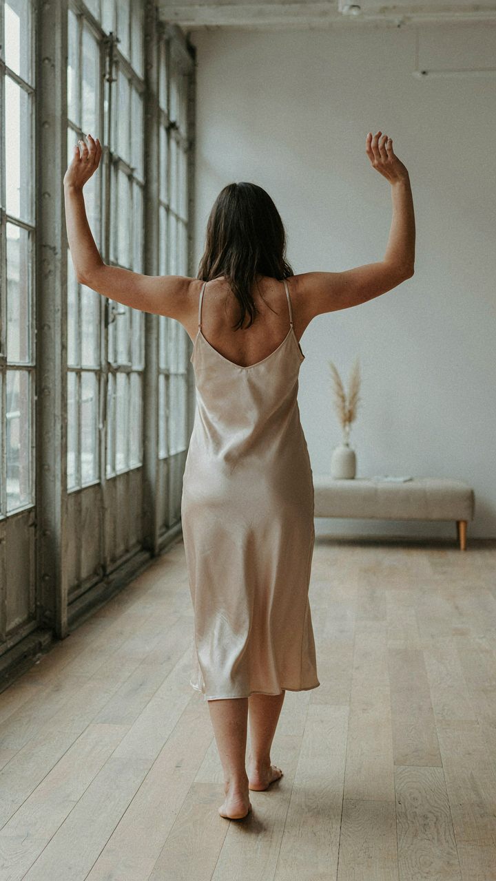 A woman in a flowing silk dress raises her arms comfortably, no pulling.