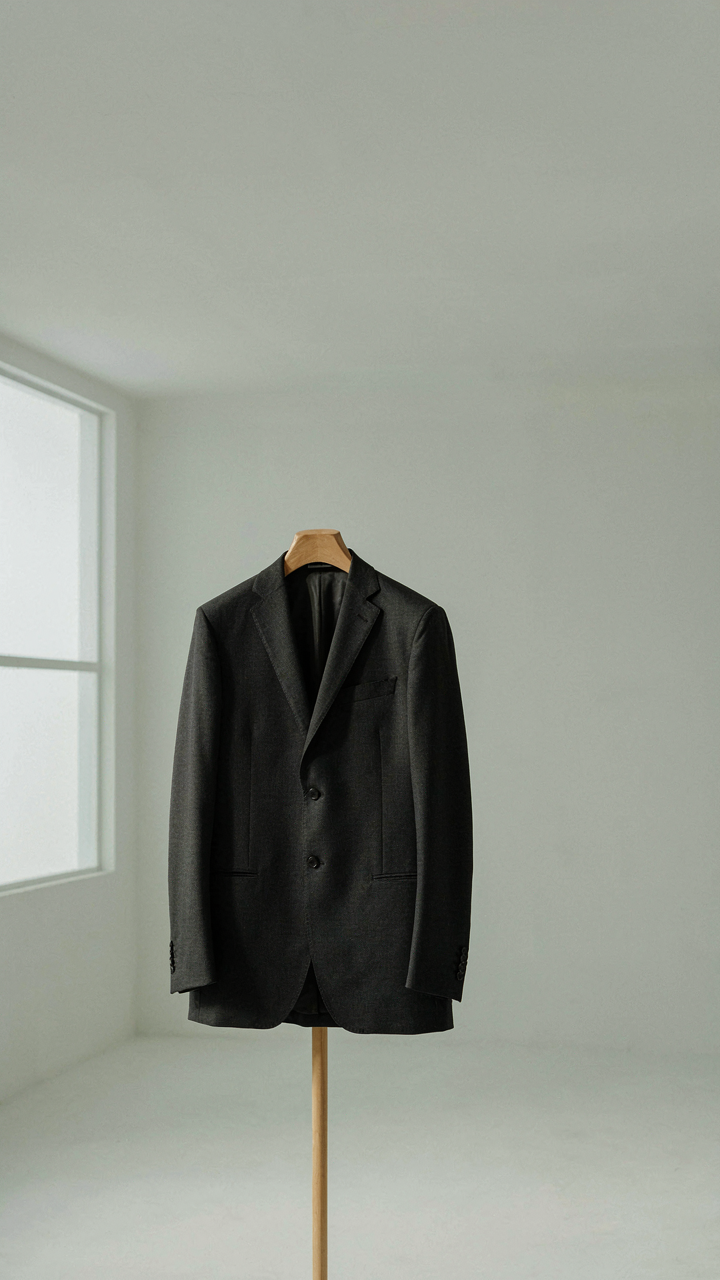 A perfectly tailored dark suit jacket hangs on a display stand, showing clean lines.