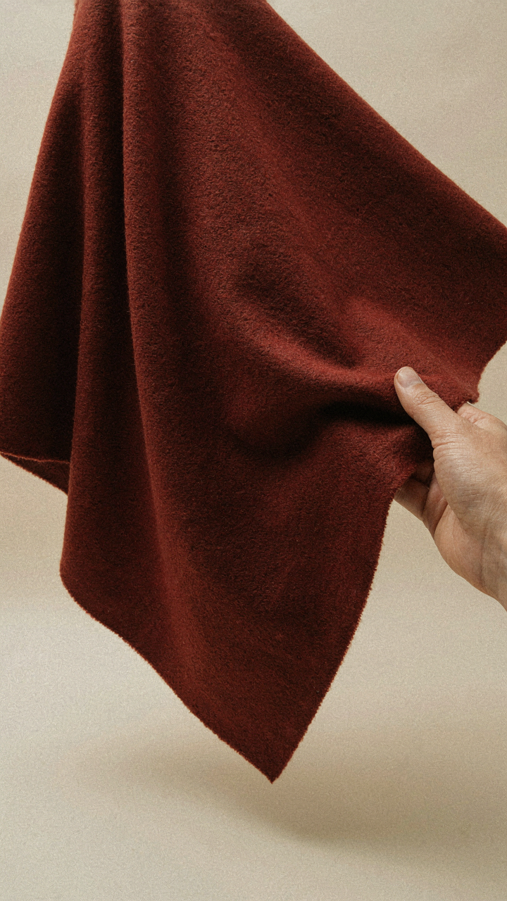 A hand holding a swatch of heavy wool fabric, showing its drape.