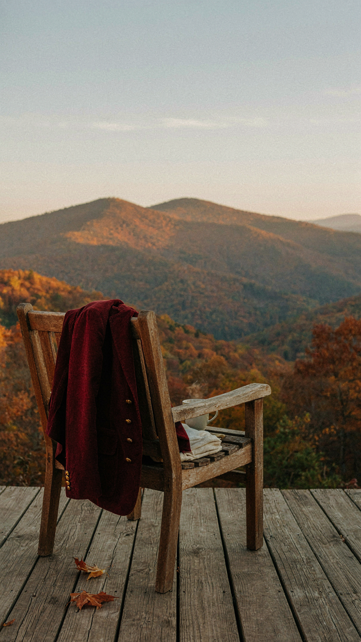 A burgundy velvet blazer drapes over a chair overlooking fall mountains.