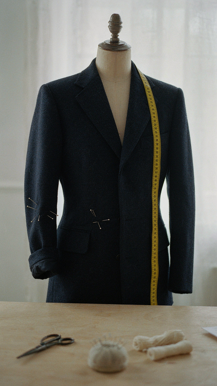 A tailor's measuring tape drapes over a dark blue blazer on a mannequin.