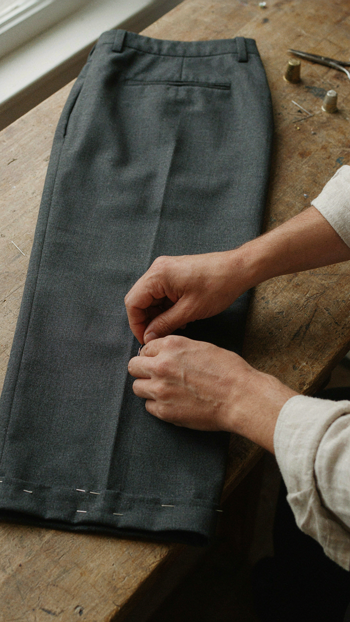A tailor's hands carefully adjusting the hem of a pair of elegant trousers.