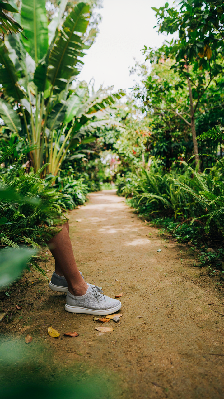Feet wearing breathable mesh sneakers on a tropical path.