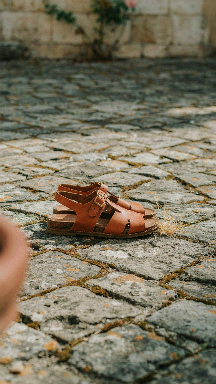 Comfortable leather sandals with arch support rest on cobblestone street.