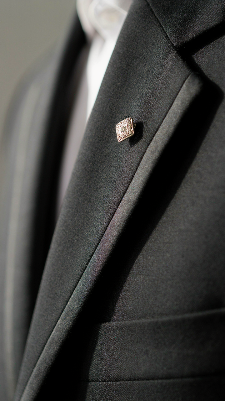 Close-up of a tailored black blazer lapel with a vintage silver brooch.