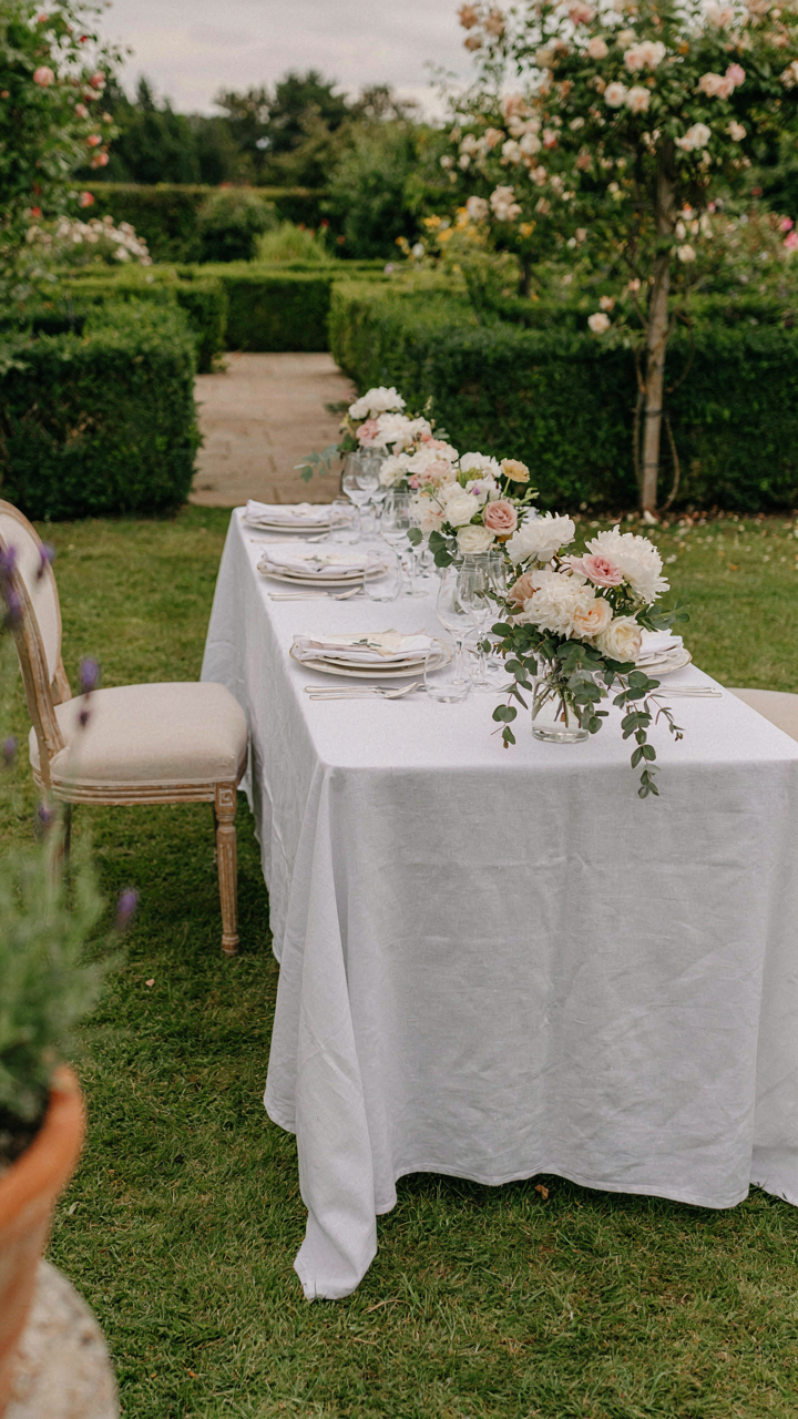 A beautifully set garden table with white tablecloths and fine china.