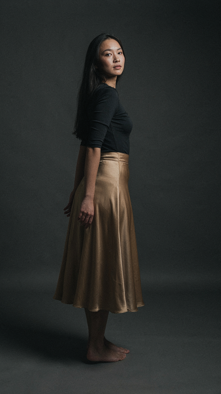 A woman wears a gold satin skirt as the focal point with a dark top.